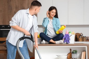 Mutfakta temizlik malzemeleri ve elektrik süpürgesi olan sevimli genç bir çift.