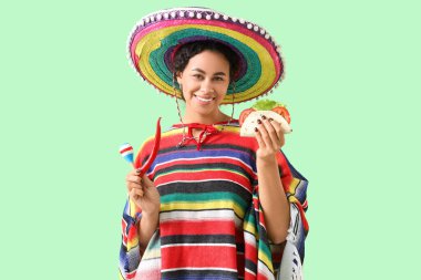 Sombrero şapkalı genç Afro-Amerikalı kadın lezzetli taco ve yeşil arka planda acı biber.