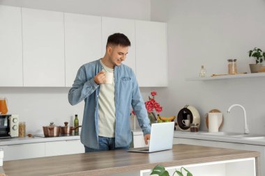 Mutfakta çay ve dizüstü bilgisayarı olan yakışıklı bir genç.