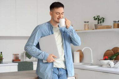 Mutfakta çay ve dizüstü bilgisayarı olan yakışıklı bir genç.