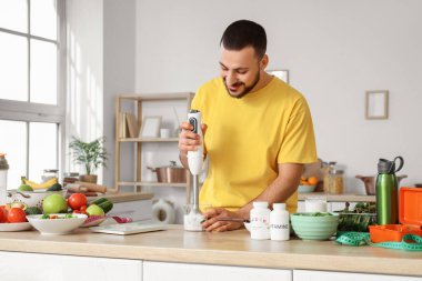 Blendırlı yakışıklı genç adam mutfakta taze sebzelerden sağlıklı meyve püresi yapıyor. Sağlıklı gıda konsepti