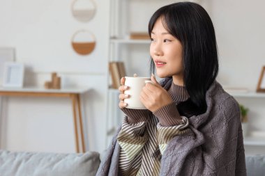 Genç Asyalı kadın, gri ekoseli ve evde bir fincan çayla