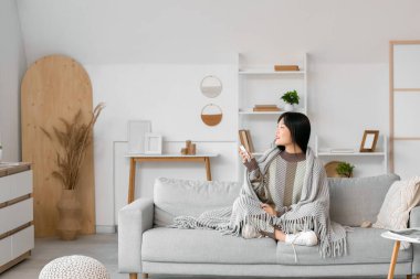 Evde klimayı açan gri ekose elbiseli genç Asyalı kadın.