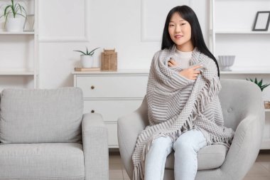 Evdeki koltukta oturan gri ekoseli genç Asyalı kadın.