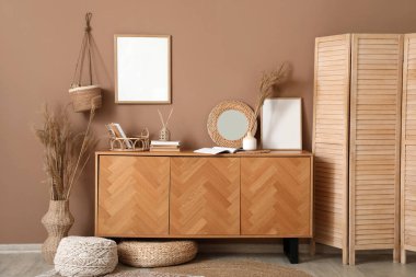 Oturma odasının içinde, bej duvarın yanında katlanan perde ve çekmeceler var.