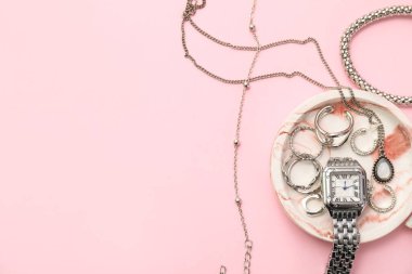Pembe arka planda gümüş mücevher ve kol saati olan tepsi.