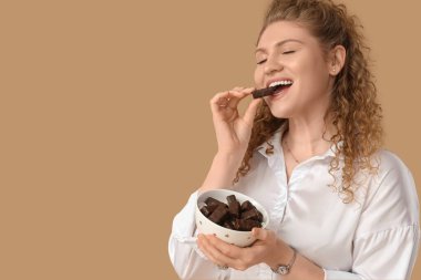 Bej arkaplanda bir kutu çikolatalı şekerle güzel bir genç kadın.