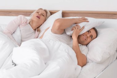 Kızgın olgun bir adam, horlayan karısıyla yatak odasında yatıyor.