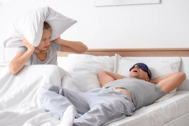 Yastıklı sinirli olgun kadın ve yatak odasında horlayan kocası.