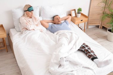 Memnun olmayan olgun bir kadın horlayan kocasıyla yatak odasında yatıyor.