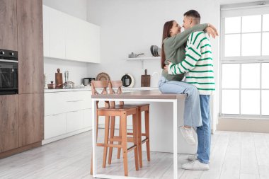 Sıcak süveter giyen sevimli genç çift evde sarılıyor.