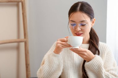 Güzel genç Asyalı kadın evde sıcak çay içiyor.