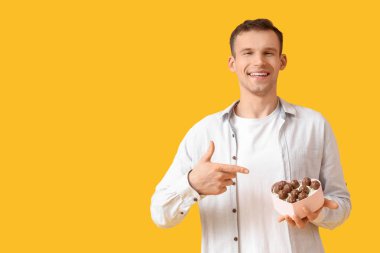 Sarı arka planda lezzetli çikolata şekerleri olan mutlu genç adam.