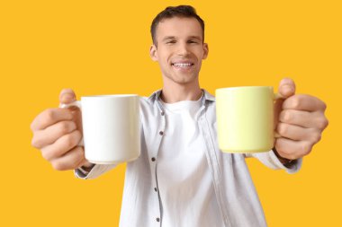 Sarı arka planda çay fincanı olan yakışıklı genç adam.