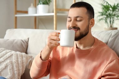 Yakışıklı genç adam çay kokusu soluyor ve oturma odasında kanepede oturuyor.