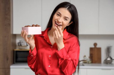 Mutfakta çikolata yiyen gülümseyen genç kadın.