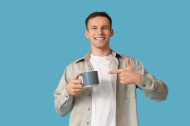 Genç adam mavi arka planda bir fincan kahveye işaret ediyor.