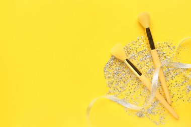 Sarı arkaplanda parıltılı makyaj fırçaları ve metin için boşluk