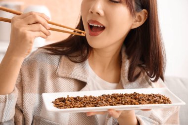 Genç Asyalı kadın evde kızarmış böcek yiyor, yakın plan.