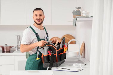 Mutfakta lavabonun yanında alet çantası olan erkek tesisatçı.