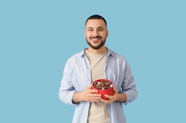 Mavi arka planda bir kutu çikolatalı genç adam.