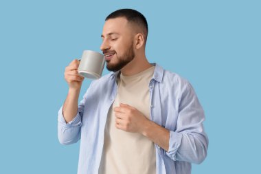 Genç adam mavi arka plandaki seramik bardaktan içiyor.