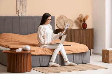 Yatak odasında doküman ve dizüstü bilgisayarla çalışan güzel genç bir kadın.