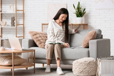 Oturma odasındaki kanepede evrak ve defterle çalışan güzel genç bir kadın.