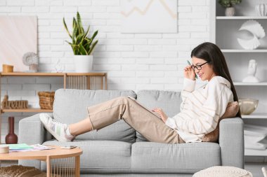 Modern tabletle çalışan ve oturma odasındaki kanepede oturan güzel genç bir kadın.