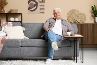 Oturma odasında kanepede oturan mutlu kıdemli adam.