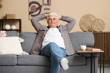 Oturma odasında kanepede oturan mutlu kıdemli adam.