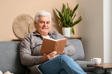 Yakışıklı son sınıf öğrencisi kitap okuyor ve oturma odasında kanepede oturuyor.