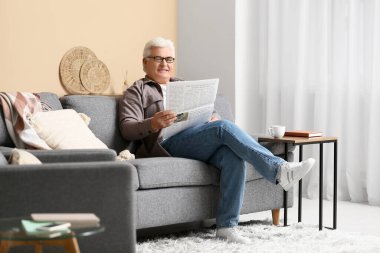 Yakışıklı son sınıf öğrencisi gazete okuyor ve oturma odasında kanepede oturuyor.