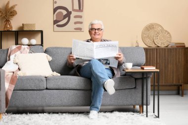 Yakışıklı son sınıf öğrencisi gazete okuyor ve oturma odasında kanepede oturuyor.