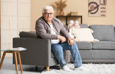 Oturma odasında kanepede oturan mutlu kıdemli adam.