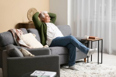 Oturma odasındaki kanepede oturan yakışıklı kıdemli adam.