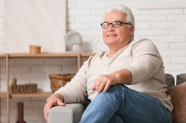 Oturma odasında kanepede oturan mutlu kıdemli adam.