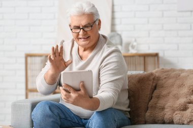 Modern tabletli yakışıklı adam oturma odasındaki koltukta oturuyor.