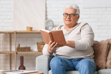 Yakışıklı son sınıf öğrencisi kitap okuyor ve oturma odasında kanepede oturuyor.