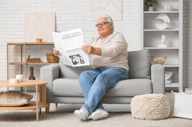 Yakışıklı son sınıf öğrencisi gazete okuyor ve oturma odasında kanepede oturuyor.