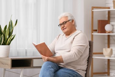Yakışıklı son sınıf öğrencisi kitap okuyor ve oturma odasında sandalyeye oturuyor.