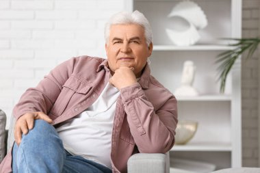 Oturma odasındaki kanepede oturan yakışıklı kıdemli adam.