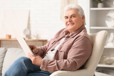 Evdeki koltukta oturan gazeteli yakışıklı adam.