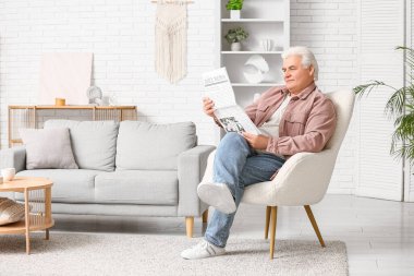 Yakışıklı son sınıf öğrencisi gazete okuyor ve evdeki koltukta oturuyor.