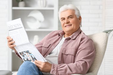 Evdeki koltukta oturan gazeteli yakışıklı adam.