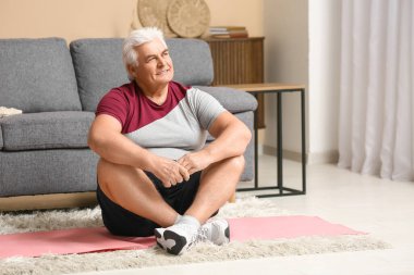 Yakışıklı son sınıf öğrencisi oturma odasında yoga minderinde oturuyor.