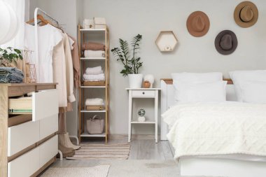 Konforlu yatak, raf ünitesi ve modern yatak odasında giysi dolu raflar.