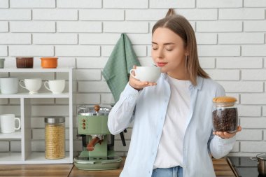 Mutfakta bir fincan sıcak kahve ve bir kavanoz fasulye ile güzel genç bir kadın.