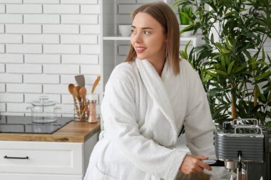 Güzel genç bir kadın, mutfakta kahve makinesiyle kahve yapıyor.