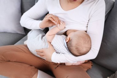 Evdeki kanepede oturmuş bebeğini emziriyor.